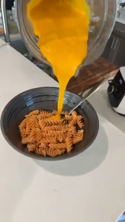 Chef Mario pouring fresh whole-food cheese sauce over pasta at a live tasting