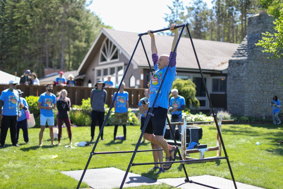 Competitor doing pull-ups as a crowd of retreat guests in matching shirts cheers at the 2026 Vegan Olympics