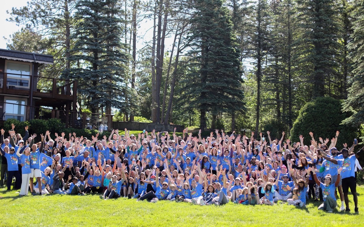 Hundreds of Vegan Wellness Retreats guests in blue shirts with hands raised for the group photo