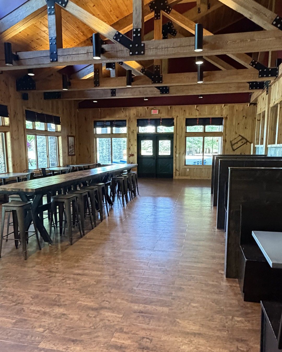 Indoor space at Timber Wolf Lake in Michigan: timber trusses, long high-top tables with stools, and booths